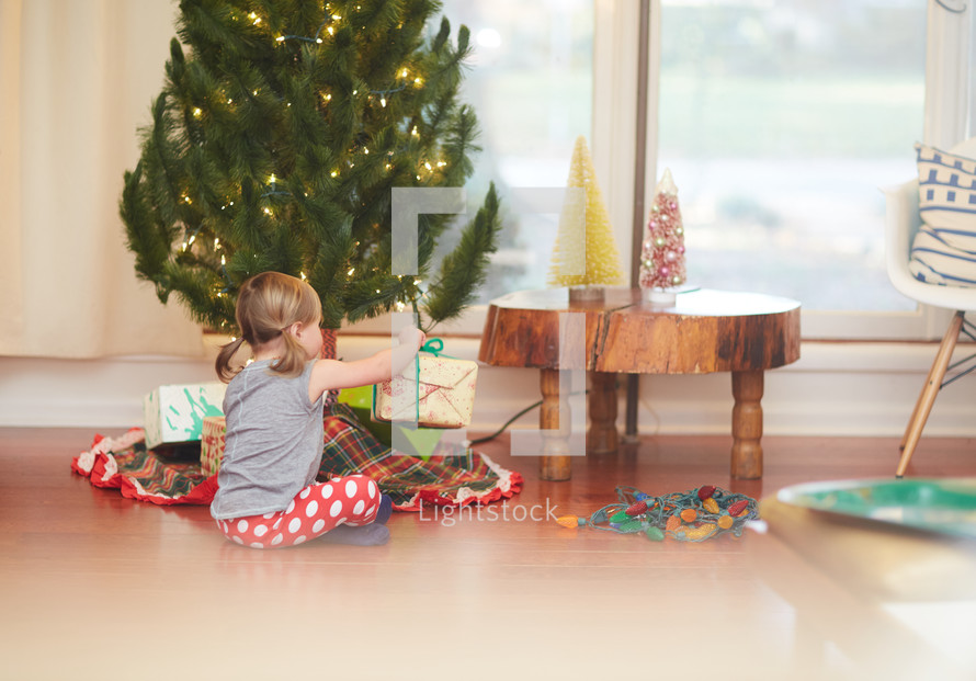 a girl opening a present under a Christmas tree