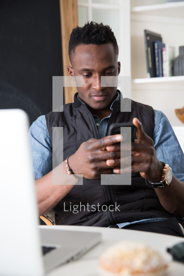 a man sitting in front of a laptop checking his cellphone 