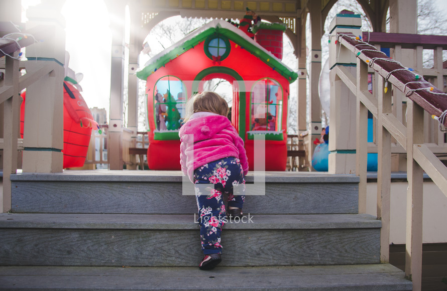 toddler girl climbing up steps to a Christmas display 