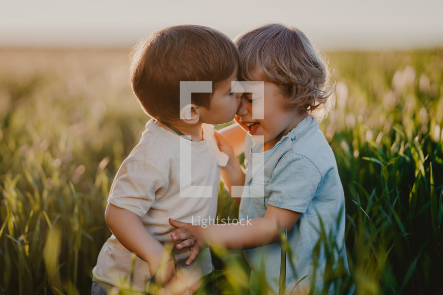 Amazing portrait of kissing kids standing in fresh green field. Lovely toddlers friends brothers, love, family, care about each other. Childhood, future, ecology concept. High quality photo