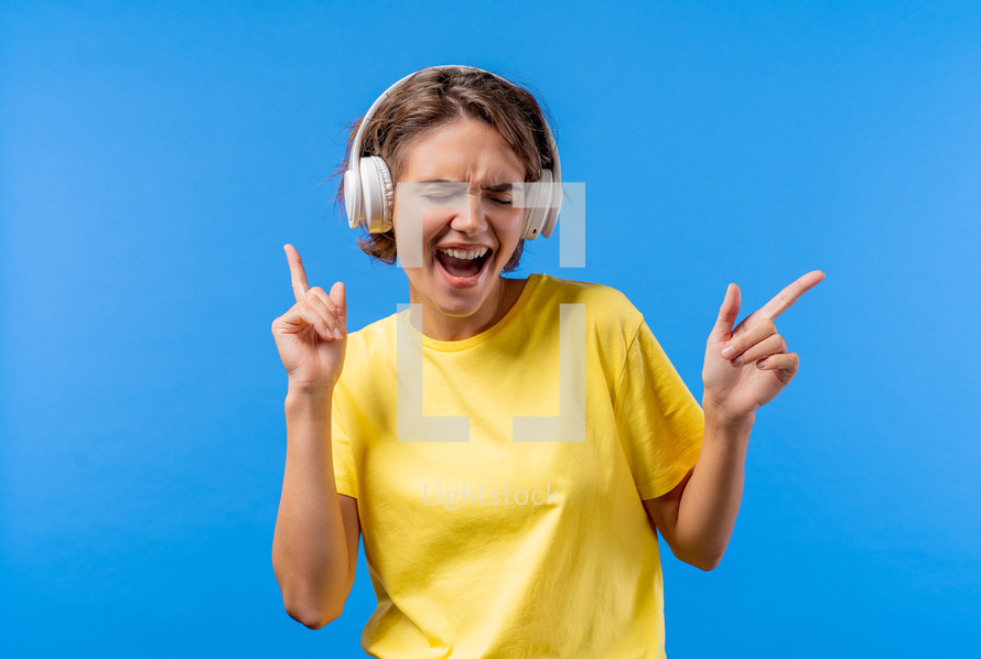 Positive woman listening music, enjoying with headphones on blue studio background. Radio, wireless modern sound technology, online player. High quality photo