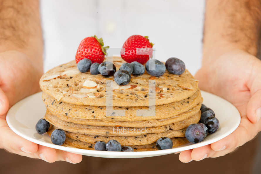 Hands holding a plate of almond pancakes covered in berries.