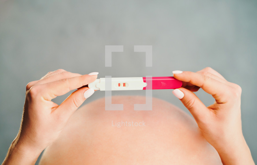 Woman holding pregnancy test on pregnant belly background