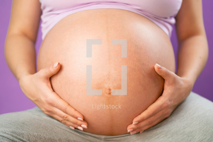 Pregnant woman holding her hands on tummy belly. Young girl expecting baby on pink bakcground. Maternity, motherhood, pregnancy concept.
