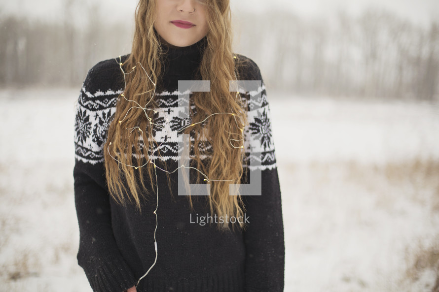 a young woman standing in the snow with Christmas lights 
