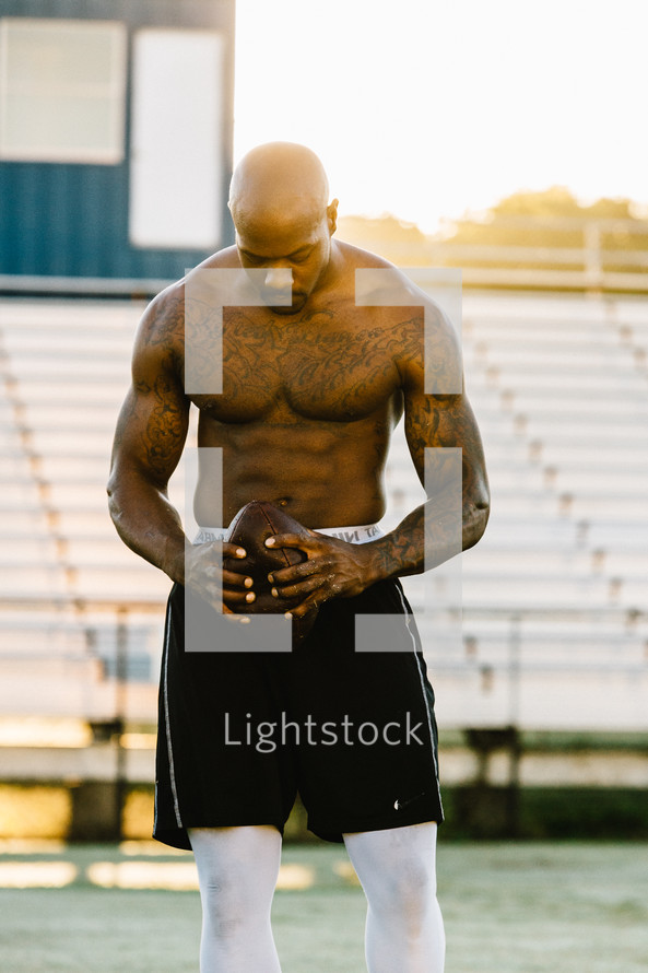 a shirtless man holding a football on a sports field 