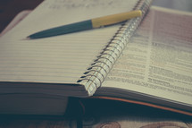 a pen and notebook on the pages of an open Bible 