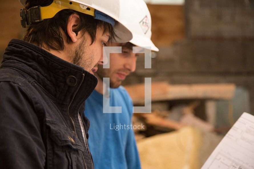 two men wearing hard hats and looking at blue prints 