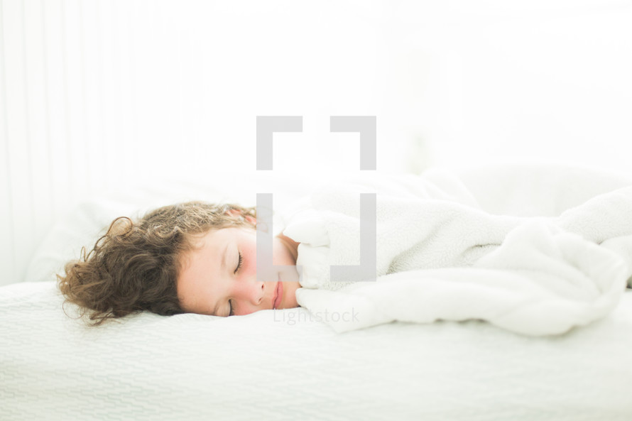 Child asleep in white bedroom with sun-kissed cheeks.