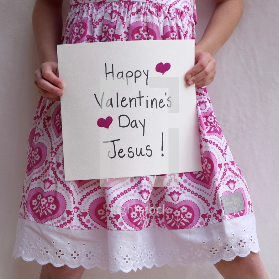 A little girl holding up a sign that reads Happy Valentine's day Jesus 