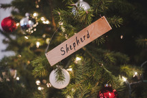 The word shepherd on a wooden Christmas ornament hanging on a Christmas tree.