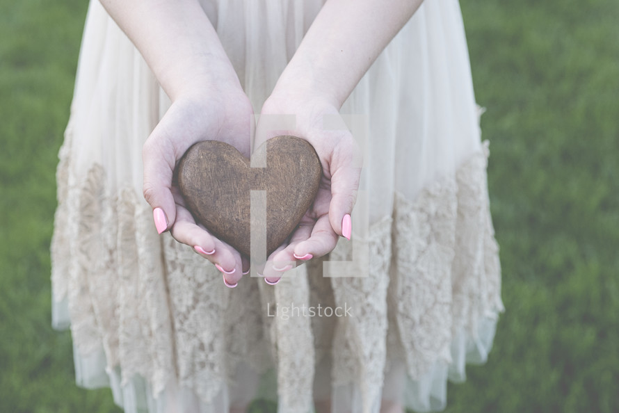 a woman holding a heart shaped stone in cupped hands 
