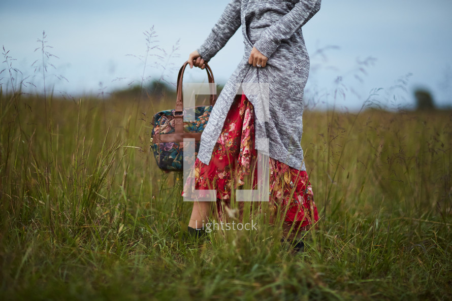 a woman standing in a field holding a purse 