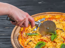 Steel pazza cutter. cutting tasty italian dish on wooden stand isolated. woman's hand with a knife cut the pizza on white background close-up