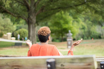 a woman sitting on a park bench with raised hands praying to God 