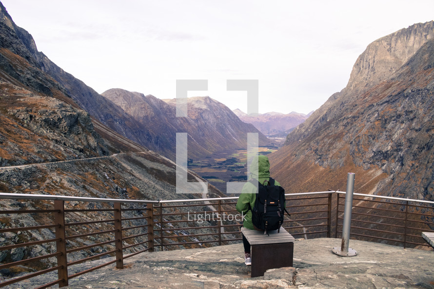 a woman sitting on a bench at a lookout site viewing mountains and valleys 