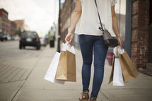 a woman walking down a sidewalk carrying shopping bags 