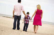 Back view of a father, son and mother walking on beach