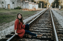 portrait of a young woman in an orange shawl sitting on train tracks 