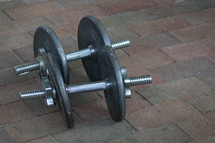 Dumbbell weights on a brick floor.