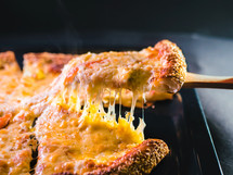 Cut off a slice of pizza. Melted cheese stretches from the piece. High quality photo