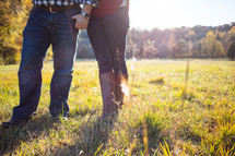 Couple holding hands as they walk through a field of grass.