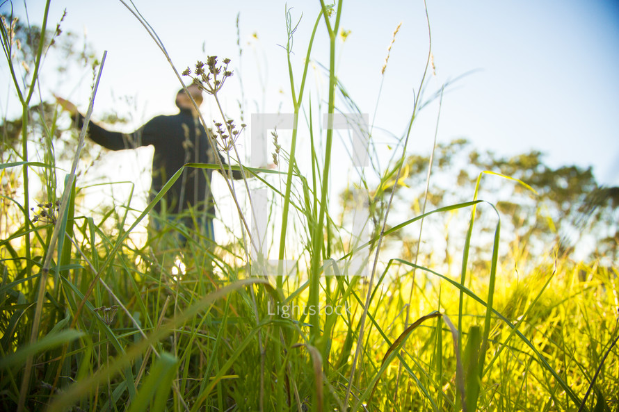 man with outstretched arms standing in tall grass 