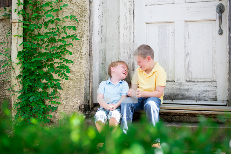 brothers laughing together sitting on steps outdoors 