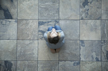 Aerial view of a woman on her knees in prayer on tiles.