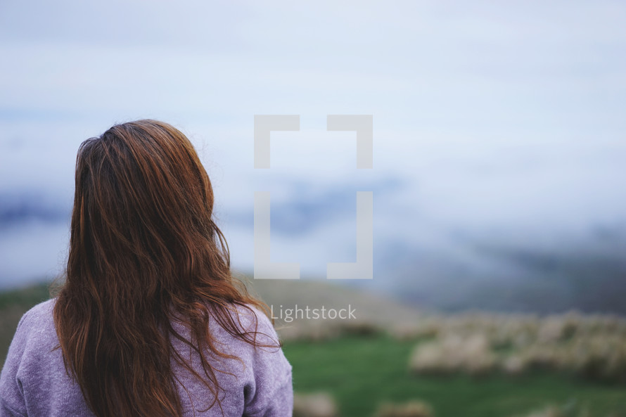 a woman looking out at clouds over a valley 