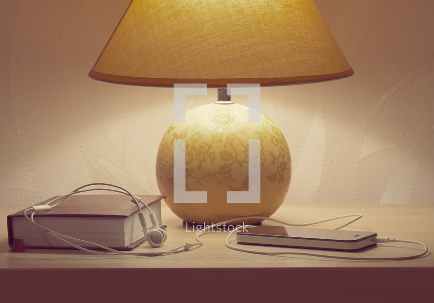 lamp, Bible, cellphone and earbuds on a nightstand 