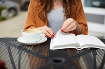 a woman sitting at an outdoor table reading a Bible 