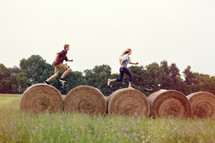 man and woman running on hay bales 