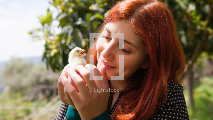 Young woman red hair holds a chick in her hands