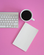 coffee mug, notebook, computer keyboard on a desk 