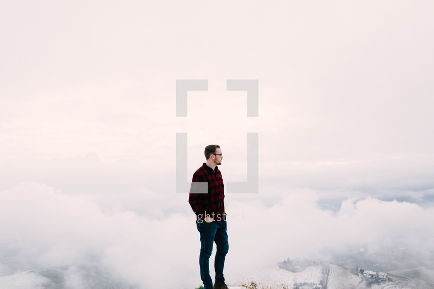 A man standing atop a mountain overlooking clouds.