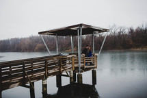 A man and woman standing together on a pier over a lake.