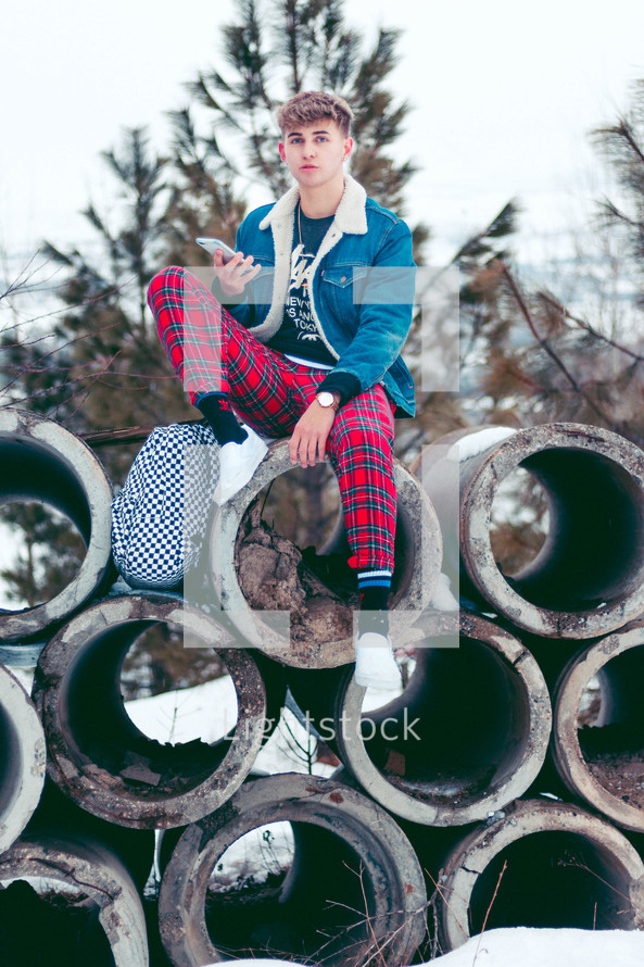 teen boy sitting on concrete pipes in winter snow 
