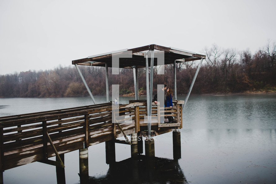 A man and woman standing together on a pier over a lake.