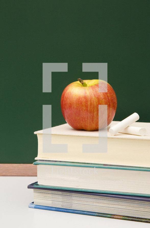 apple on a stack of books and chalkboard and chalk 