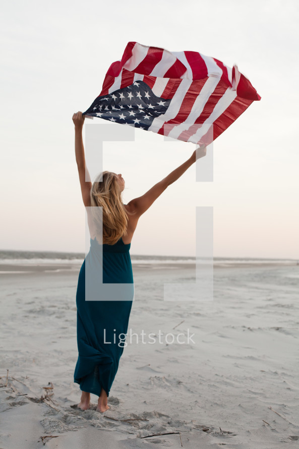 woman holding up an American flag on a beach 
