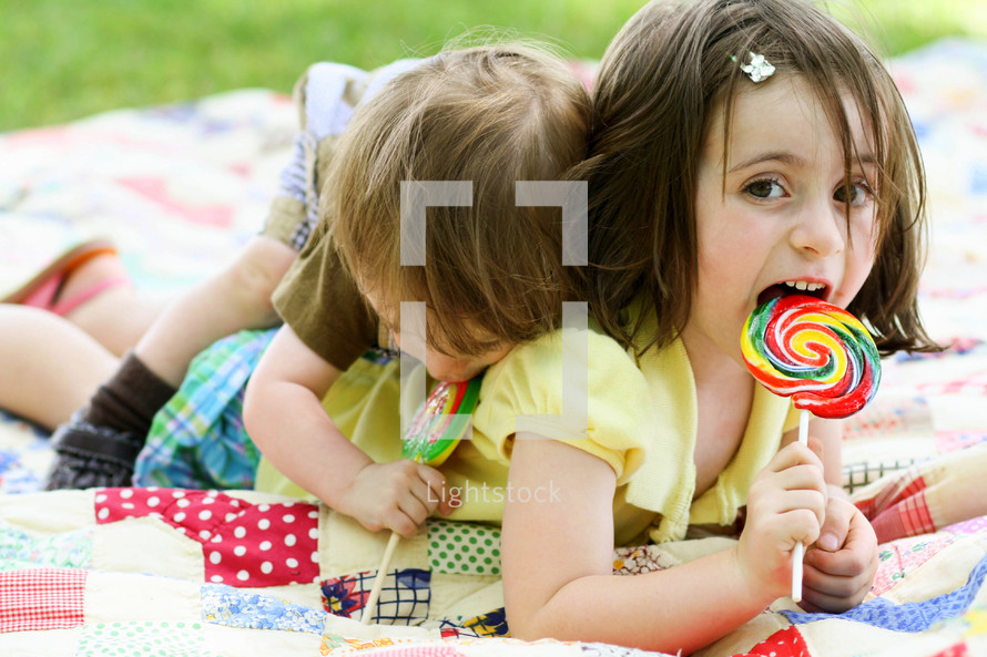 children licking suckers on a blanket outdoors 
