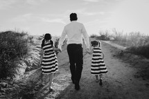 a father holding hands with his daughters as they walk up a sand dune 
