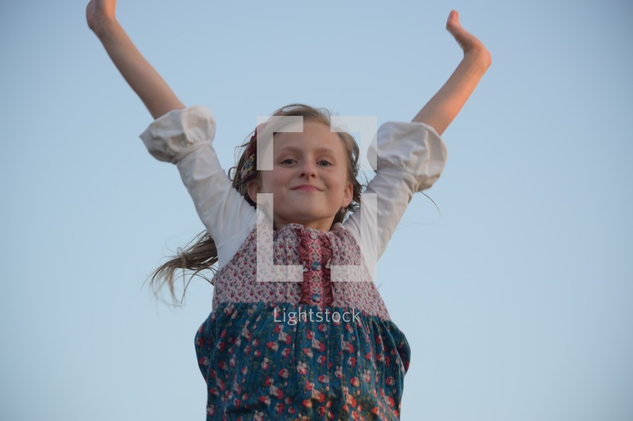 a little girl with raised arms against a blue sky 