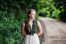 young woman with braided hair standing outdoors on a dirt road 