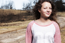Smiling girl standing outside by a dirt road.