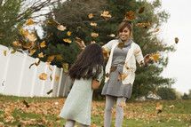 Mother and daughter playing in the fall leaves in the back yard.
