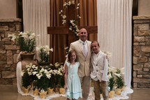 A father and his children on Easter Sunday standing in a church narthex in front of a cross and Easter lilies 