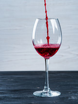 Red wine being poured into wine glass on white background. Minimalist style, black shabby vintage wooden table.