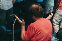 an elderly woman sitting with hands raised during a worship service 